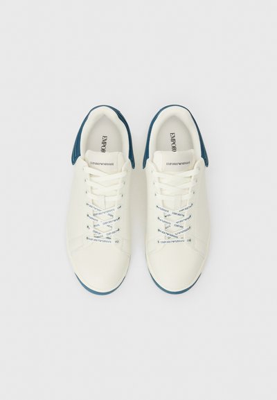 Vita lädersneakers med blå texturerad häl och blå snören med upprepad branding. Rund tå och slät gummisula.