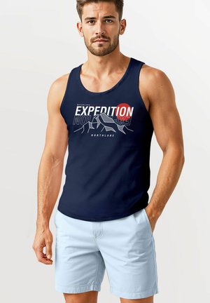Dunkelblaues Tanktop mit dem grafischen Text "EXPEDITION" in Weiß und Rot. Kombiniert mit hellblauen Shorts. Der Stoff wirkt weich und hat eine lässige Passform.