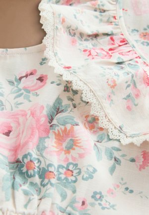 Virágos szövet pasztell rózsaszín, őszibarack és kék virágokkal, finom fehér csipke díszítéssel egy fodros szél mentén.