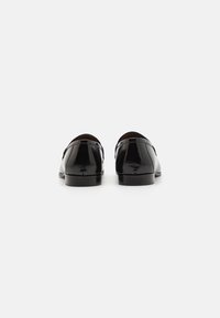 Mocasini din piele neagră cu ofinisaj lucios, vârf rotund, toc mic și decorativ cusut pe spate.