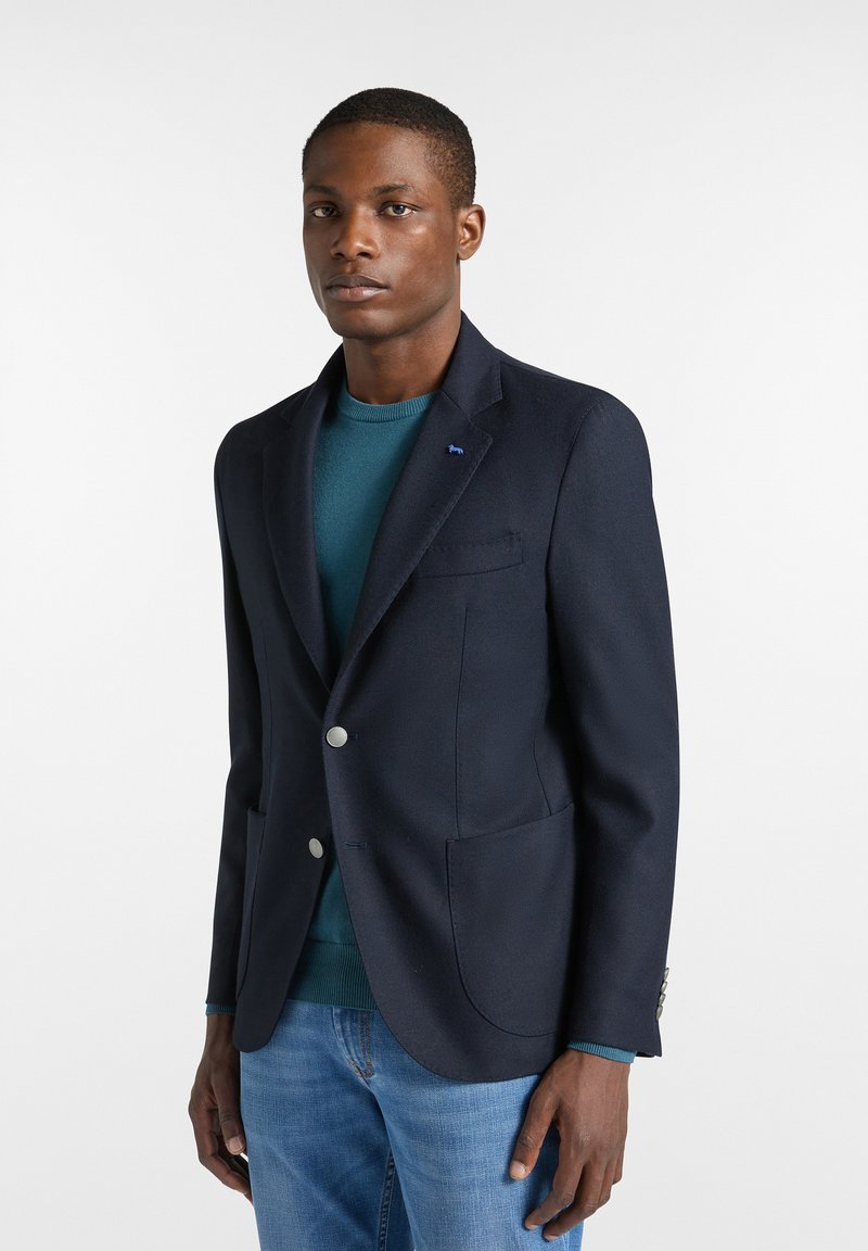 Navyblå blazer i slätt tyg, enfärgad med två silverknappar, med bröstficka och sidfickor. Bärs över en tealtröja.