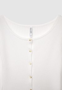 Haut en maille côtelée blanche avec un col rond, présentant six boutons ronds de couleur claire et une étiquette en tissu indiquant la taille « S ».