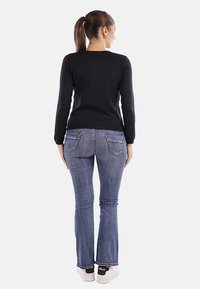 Top nero a maniche lunghe, aderente in vita. Jeans blu a palazzo con tasche posteriori, lavaggio chiaro, indossati con sneakers bianche con dettagli neri.
