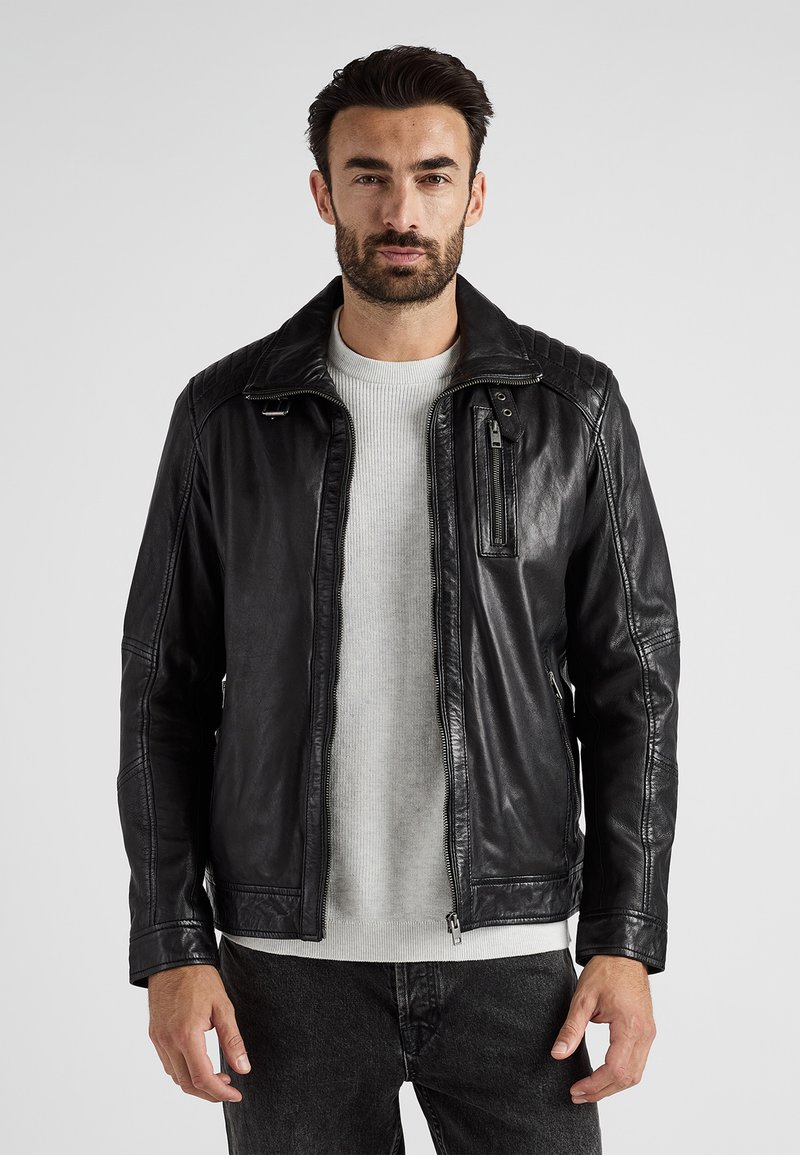 Svart läderjacka med ribbad axeldesign, hel dragkedja och sidoficka. Buren över en ljusgrå tröja.