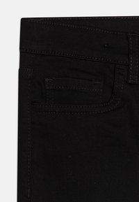 Jeans in denim nero con una trama liscia, un design tradizionale a cinque tasche e cuciture a contrasto. Presentano una piccola tasca anteriore.
