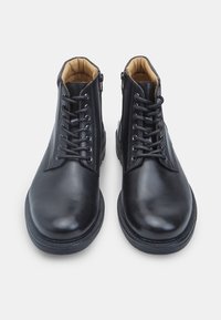 Stivali ankle in pelle nera con finitura liscia, dotati di allacciatura frontale, zip laterale e un interno imbottito color beige. Suola in gomma piatta.