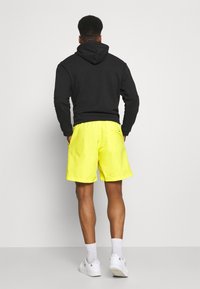 Black hoodie, yellow shorts, elastic waistband, two pockets, white socks, and white sneakers. Simple design with vibrant color contrast.