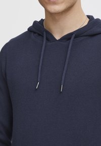 Sudadera azul marino hecha de tejido de punto, con capucha ajustable, ribete acanalado y agujas en tono plateado en los cordones.