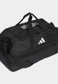 Black duffel bag made of durable fabric, featuring white Adidas logo and three stripes on the top, with dual carrying handles and zipper closure.