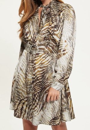 Femme portant une robe à manches longues ceinturée avec un motif animalier marron, beige et blanc et un col noué.