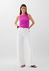 Top a compressione a coste di colore rosa brillante, abbinato a jeans bianchi a gamba larga. Dettagli notevoli includono vita alta e accenti a bottone.