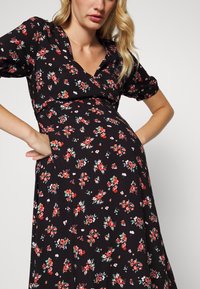 Vestido preto floral com decote em V, mangas curtas bufantes e cintura ajustada, adornado com padrões vibrantes de flores vermelhas e verdes.