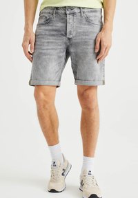 Grå denimshorts med uppvikta nederkanter, fem fickor och en blekt finish. Kombineras med beige sneakers och vita strumpor.