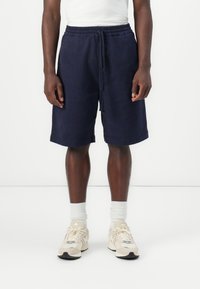 Pantalones cortos de algodón azul marino con cintura elástica y cordón. Presentan bolsillos laterales y un corte recto, combinados con calcetines blancos y zapatillas.
