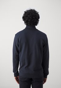 Marinblå sweatshirt med hög krage, lång ärm och mjuk textur. Har en avslappnad passform och ribbade muddar och nederkant.