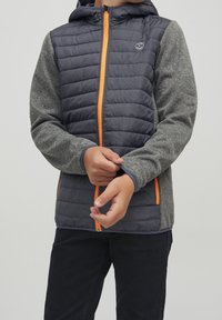 Padded jacket w kolorze szarym i granatowym, z kapturem, pomarańczowym zamkiem błyskawicznym oraz szarymi rękawami o teksturowanym wykończeniu.