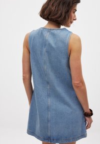 Jeanimekko, jossa on hihaton muotoilu, vaaleansininen väri ja suora leikkaus. Näkyvää ompelua selkäsaumassa ja helman yläosassa.