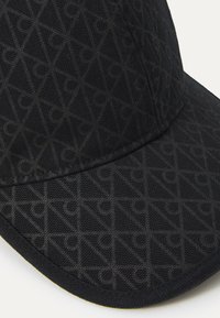 Black cap featuring a textured pattern with geometric shapes. Made of fabric with a smooth finish and stitched edges.