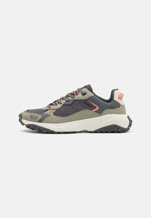 Sneaker mit niedrigem Schaft in Olivgrün, dunkelgrauem Mesh, korallenroten Akzenten, dicker weißer Sohle und robustem schwarzem Profil, Seitenansicht vor weißem Hintergrund.