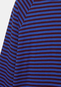 Close-up af stof med vandrette blå og mørkerøde striber, der danner et chevronmønster ved skuldersømmen.