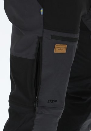 Black and dark gray ski pants with zippered pockets, a brown leather SWEDEMOUNT patch, and a Swedish flag detail on the side.