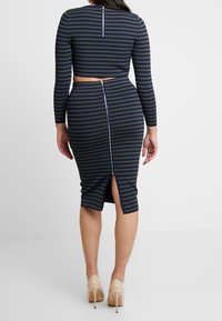 Raidallinen kaksiosainen asu, johon kuuluu lyhyt pitkähihaisen yläosan ja polvipituinen hame. Värit ovat laivastonsininen ja oliivinvihreä, selässä halkio ja vetoketju.