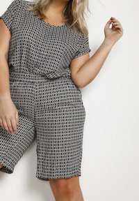 Combinaison à motifs noir et blanc à manches courtes, avec un design géométrique, taille élastique et shorts arrivant au genou. Tissu texturé.