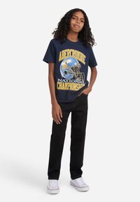 Camiseta gráfica azul marino con un diseño de casco de fútbol y el texto "Campeonato Nacional Abercrombie", combinada con pantalones negros y zapatillas blancas.