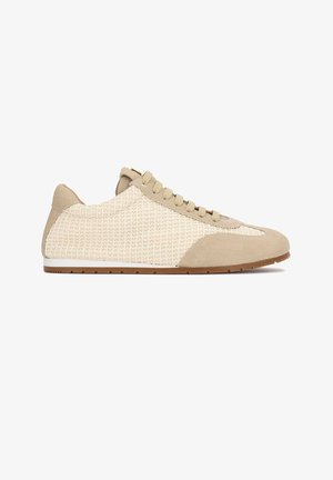 Zapatilla baja beige con tejido tramado texturizado, superposiciones de ante en la puntera y el talón, cierre de cordones y suela de goma marrón.