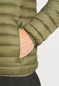 Pufferjack in olijfgroen, doorgestikt ontwerp met horizontale naden, voorzien van een zijzak en een aansluitende manchette. Glad, lichtgewicht stof.