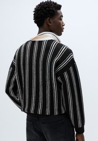 Maglione a maglia a righe bianche e nere con ampio collo, caratterizzato da tessuto strutturato e spalle scese. La vista posteriore mostra un motivo a righe a contrasto.