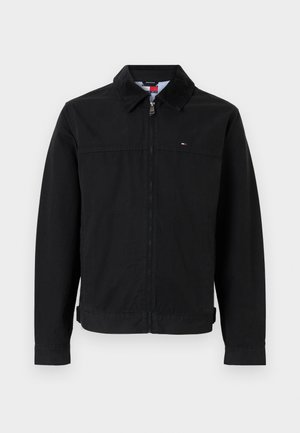 Fekete kabát gallérral, elülső cipzárral és oldalzsebekkel. Simább anyagból készült, kis logóval a mellkason.