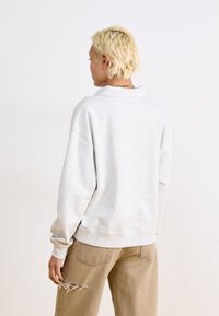 Svetlo šedý oversized sweatshirt s golierom, s rebrovanými manžetami a spodným okrajom. Skombinovaný s svetlo hnedými nohavicami s ošúchaným detailom.