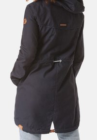 Voděodolná tmavě modrá bunda s kapucí, stahováním v pase a logem na rameni. Texturovaná látka s délkou sahající do poloviny stehen.