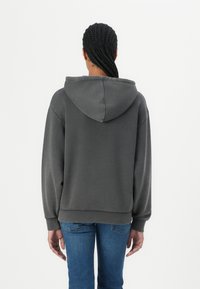 Hoodie gris foncé avec une coupe décontractée, manches longues et capuche à cordon. Le sweat-shirt présente des poignets et un ourlet côtelés, ainsi qu'une texture de tissu lisse.