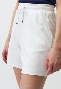 Shorts bianchi in cotone con vita regolabile tramite coulisse, tasche laterali e finiture metalliche sulle estremità della coulisse, caratterizzati da una texture liscia.