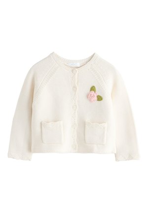 Kremowy sweterek dla dziecka na guziki, z dwiema małymi kieszonkami i różowym kwiatem z zielonymi liśćmi wyszytymi na piersi.