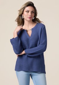Pulover tricotat albastru cu decolteu în V, având un accent metallic la gât și mâneci lungi lejere. Textură moale.