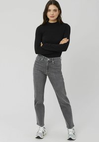 Un haut noir à manches longues associé à un jean gris taille haute et des baskets argentées. Présente un design ajusté et une légère élasticité. Look simple et moderne.