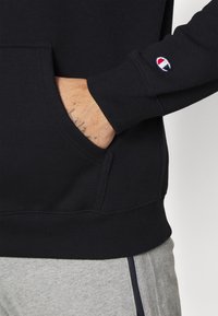 Felpa nera con tasca frontale, polsini e orlo a costine. Presenta un piccolo logo ricamato sulla manica. Tessuto morbido.
