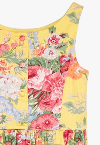 Šaty s květinovým potiskem na žlutém pozadí, obsahující růžové, červené a zelené květiny. Součástí jsou knoflíky a nařasený lem pro texturu.