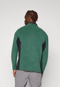 Green fleece jacket with black side panels, long sleeves, and a stand collar. Soft texture and relaxed fit, suitable for casual wear.