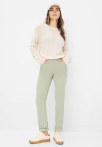 Lys beige, hyggelig strikketrøje med lange ærmer, parret med lysegrønne, tætsiddende bukser. Outfittet er suppleret med cremefarvede sneakers og en kasket.