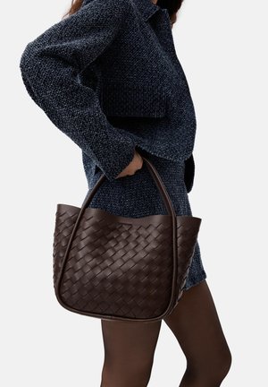 Borsa tote in pelle intrecciata marrone scuro con parte superiore arrotondata e manici robusti, esposta su uno sfondo di tessuto blu scuro texturizzato.