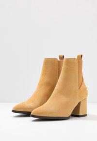 Stivali ankle in suede color beige chiaro con punta affusolata e tacco spesso. Presentano lati elastici e linguette per una facile calzata.