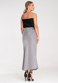 Seidiger schwarzer Oberteil mit dünnen Trägern, kombiniert mit einem fließenden grauen Satrock. Der Rock hat eine glatte Textur, reicht bis zur Mitte der Wade und wird mit schwarzen High Heels getragen.