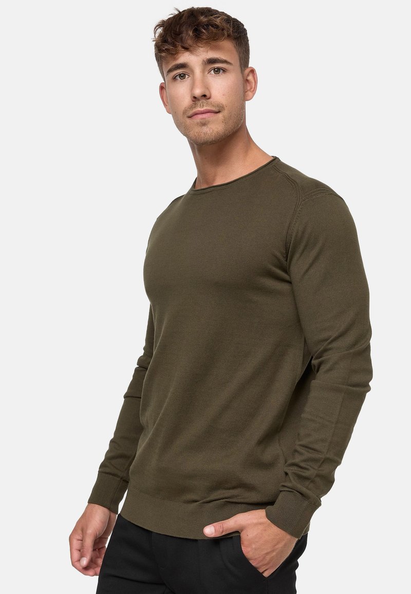 Olijfgroene lange mouw crewneck trui in ribgebreide stof met aansluitende manchetten en zoom, gedragen over zwarte broek, met een soepele stoftextuur.