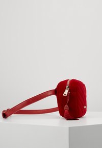 Czerwona, pikowana torebka na ramię z aksamitu, z złotym zamkiem błyskawicznym i detalem w postaci chwostu, wyposażona w płaski pasek i kompaktowy, zaokrąglony, prostokątny kształt.
