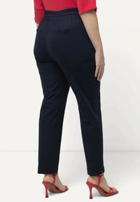 Pantalones de cintura elástica en azul marino, con bolsillos laterales, corte ajustado y textura suave. Combinados con sandalias de tacón alto rojas.
