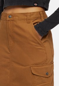 Gonna in cotone marrone con tasche laterali, chiusure a scatto in metallo e dettagli di cucitura a vista. Design semplice con silhouette dritta.